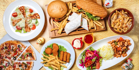A colorful table setting with pizzas, sandwiches, fries, salad, and more. Plates and bowls hold sauces, creating an inviting atmosphere.