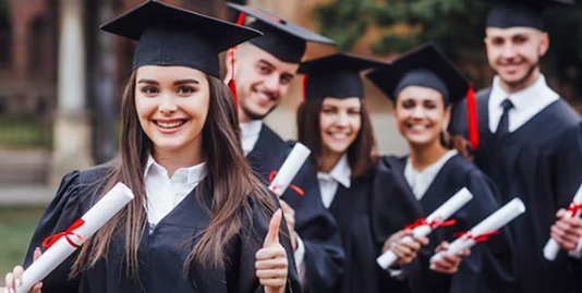 The image features jubilant graduates in caps and gowns, proudly displaying their diplomas. Among them, a confident girl gives a thumbs-up to the camera, capturing the celebratory moment of their significant achievement.